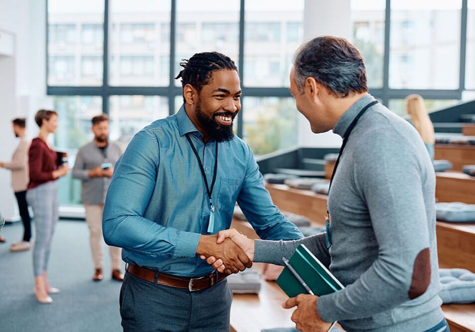 coaches-shaking-hands Two men are shaking hands in an casual networking environment while smiling at each other.
