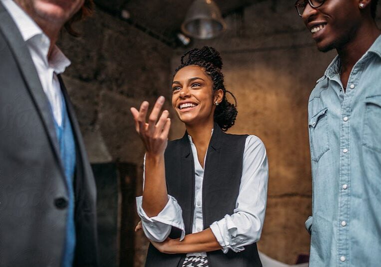 icf-about-collaborative-coaching A professional woman smiling brightly, engaged in an animated collaborative coaching session with two male colleagues who are out of focus.