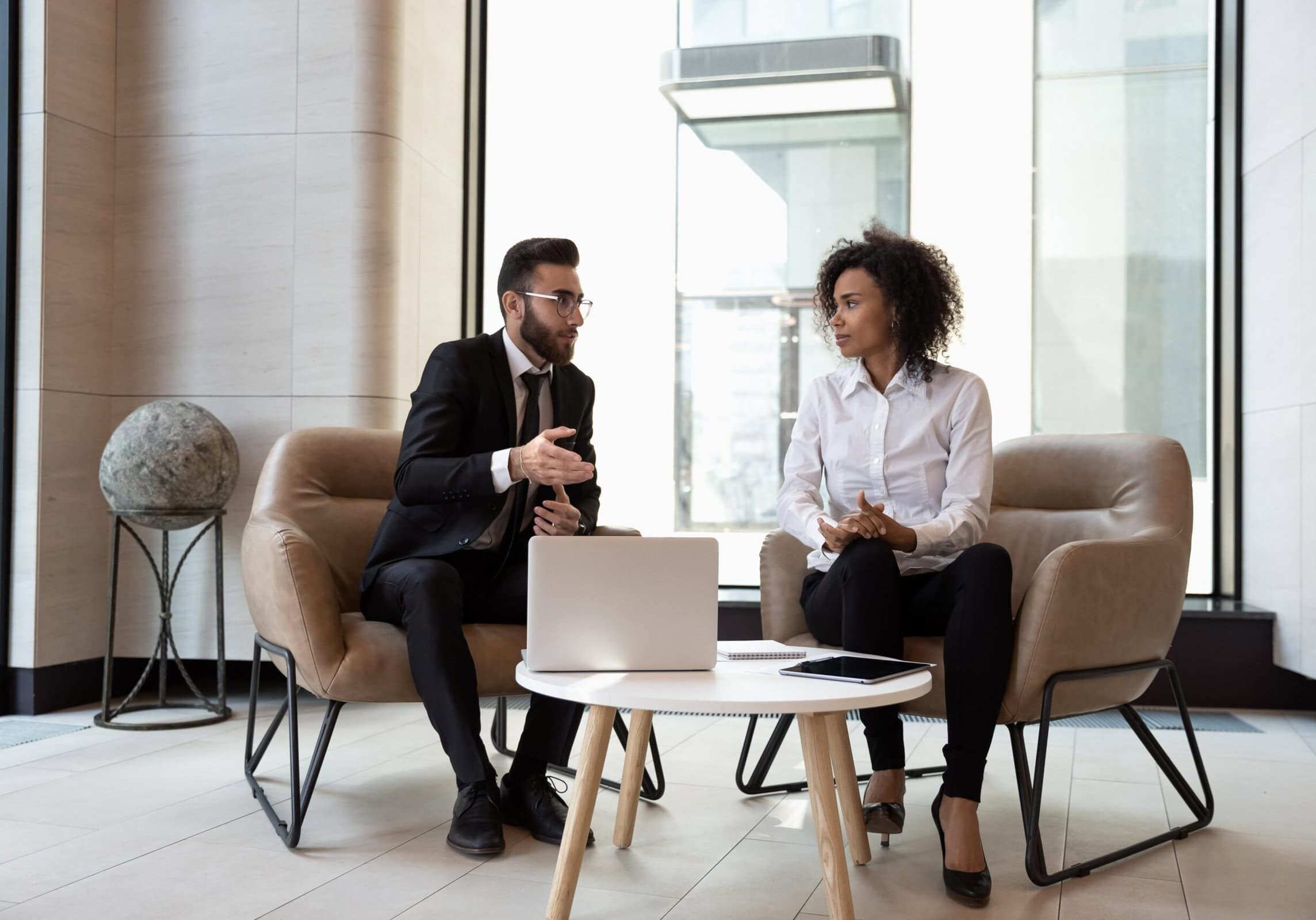Professional Coaching Session A man in a suit and a woman in professional attire seated and discussing work in a modern office setting